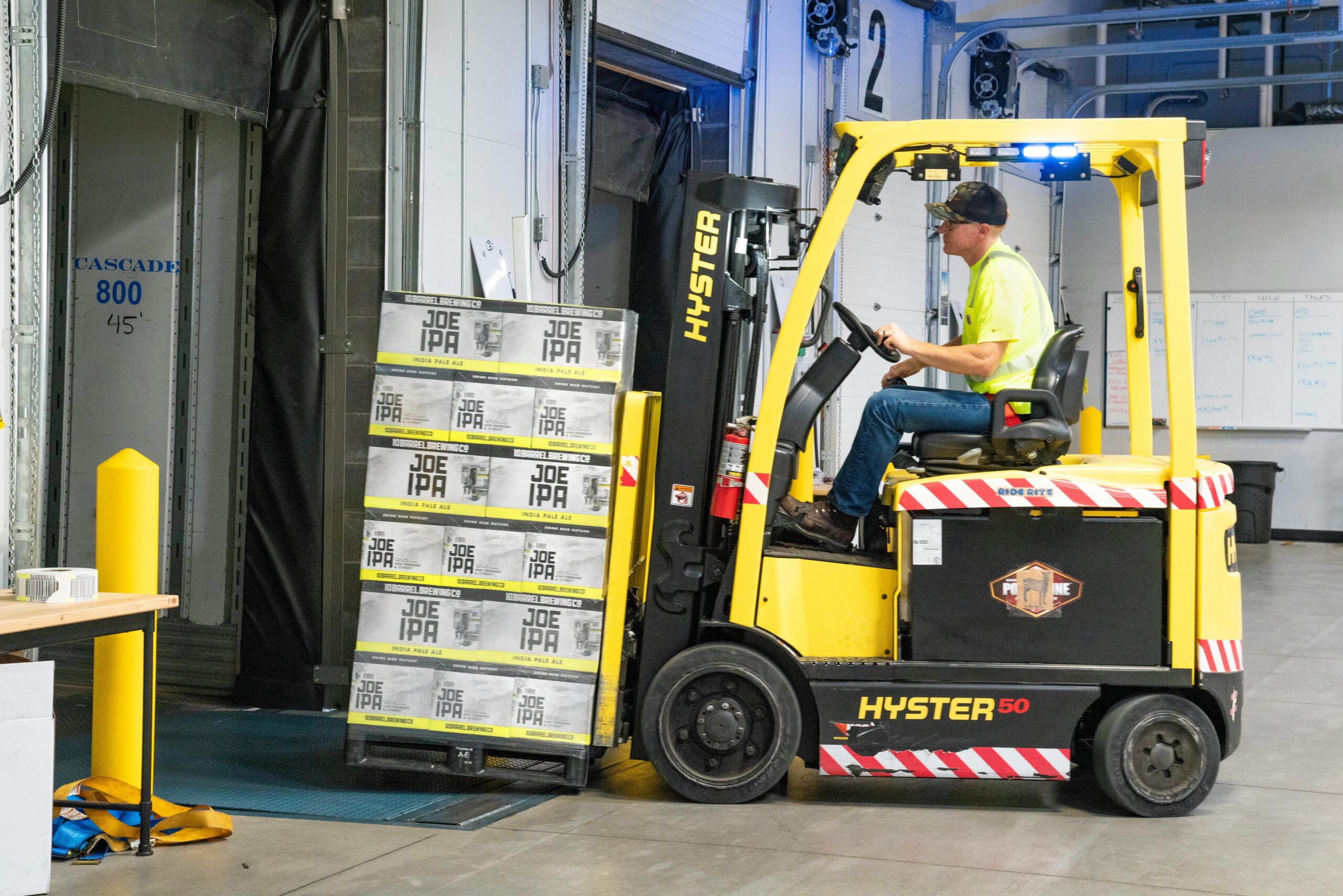 pexels-photo-1267324-1267324 A worker drives a Hyster forklift moving Joe IPA boxes in a warehouse.